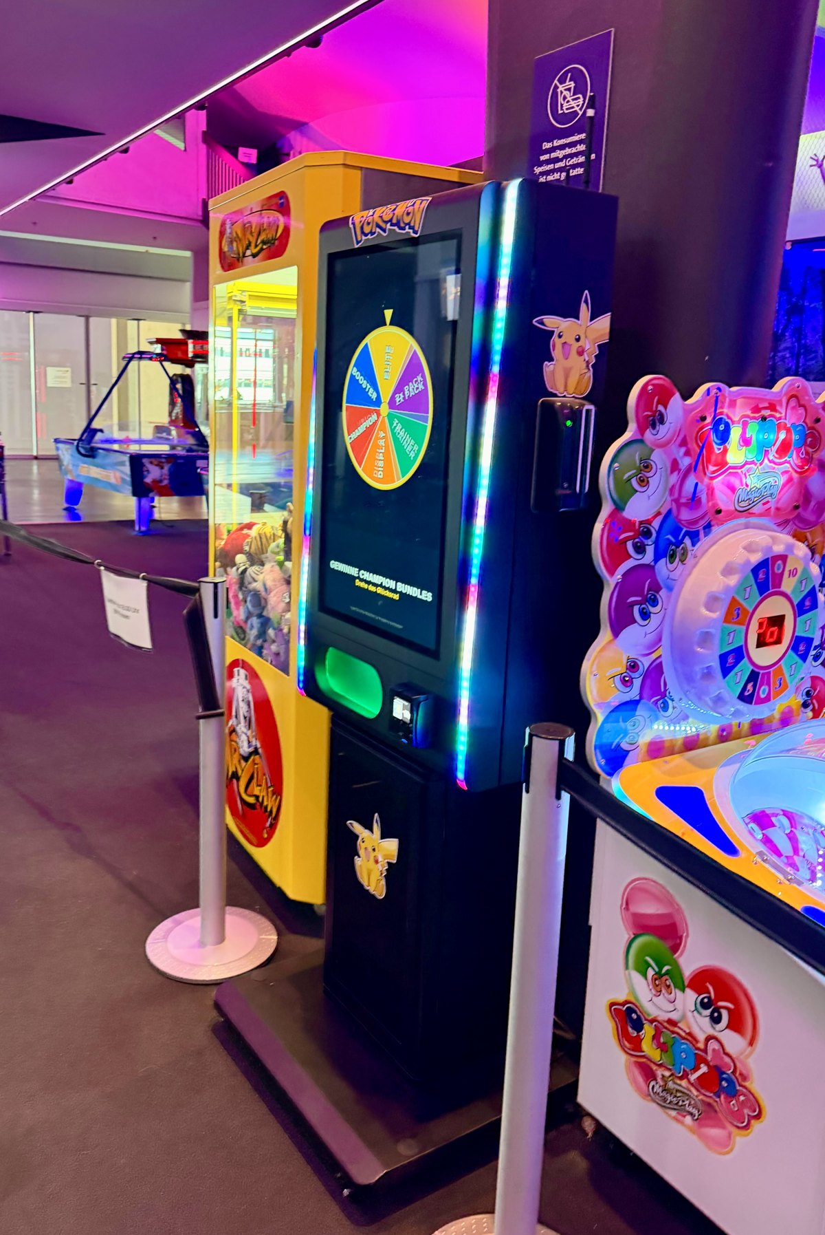 Ein Nova Pulse im Pokémon-Design auf einem Ständer in einer Spielhalle, neben einem Greifautomaten